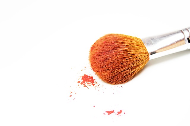 A blush brush sits on a white table with pink powder spilling from the brush